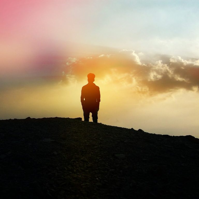 Reflective Sunset Hopeful, reflective, silhouetted figure standing on a hill against a colourful sunset sky.